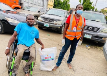 A man on a wheelchair carrying the food package and a woman standing beside him