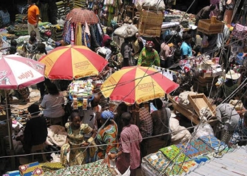 aerial view of a lot of people in close proximity in a market area. There are two big umbrellas close to each other with people under it, shading themselves from the heat of the sun
