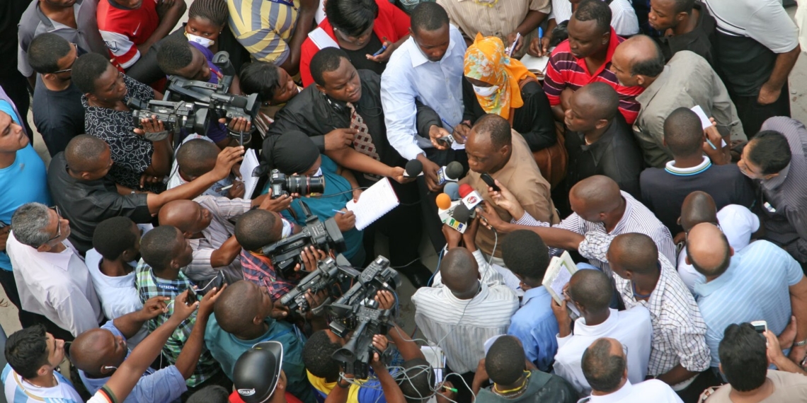 People clustered together holding microphone and recorder to indicate they are journalists