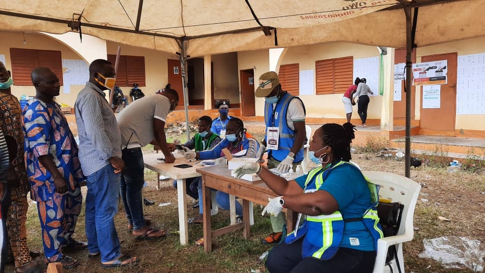 In the Image a few people are seen casting their votes under a canopy
