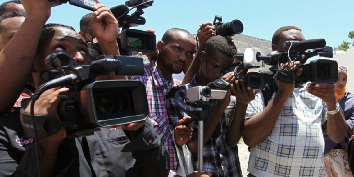 men standing outdooor holding video camera, microphone and camera