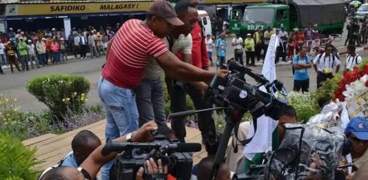 An image of a group of journalists trying to get an interview holding recorders, microphones and video cameras