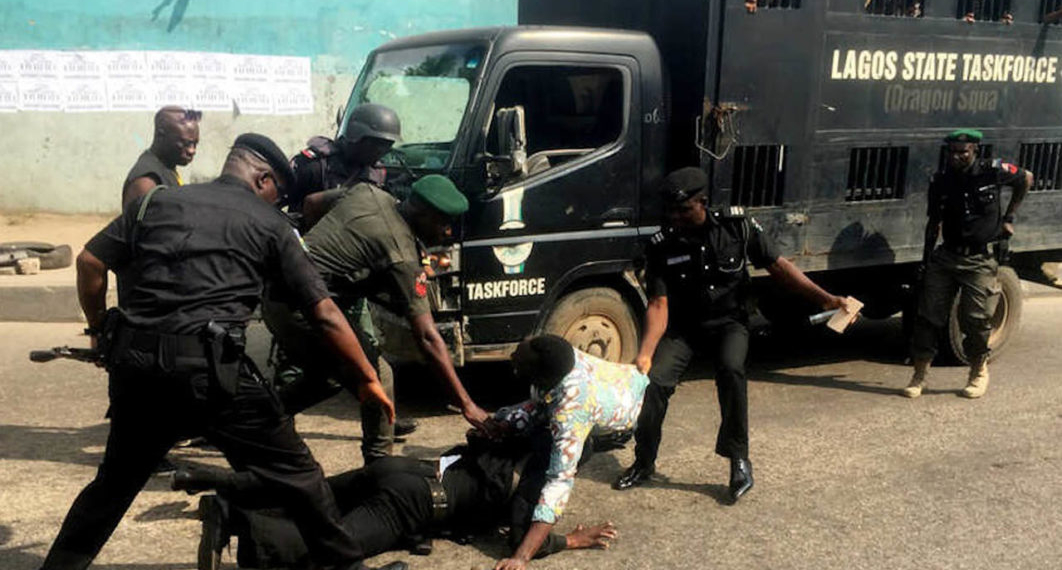 Image of Police officers harassing a man, there is a police van in the background a