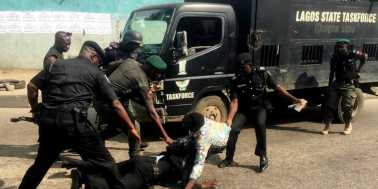 Image of Police officers harassing a man, there is a police van in the background a