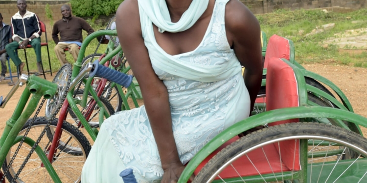 A woman on wheelchair sitting in an open field. There are people around but far away from her