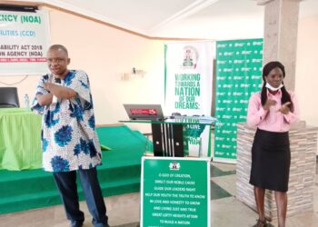 An amputee man standing and holding a microphone and a sign language interpreter doing interpretation for the Deaf participants
