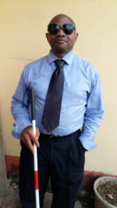 Man standing, holding a guide cane with the other hand in his pocket