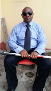 Man sitting on a chair, holding a guide cane across his leg