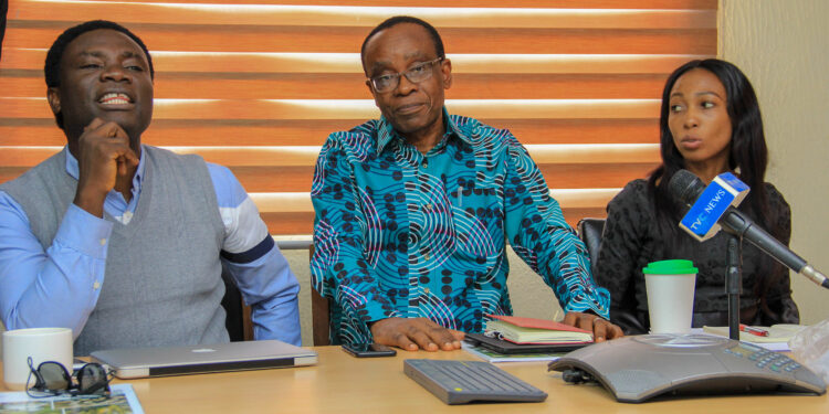 2 men and one woman seated, microphone in front of them, on a table