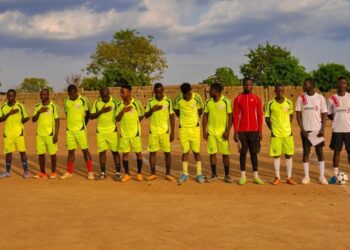 Footballers wearing yellow standing on a line on a football pitch, with their coach