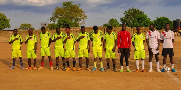 Footballers wearing yellow standing on a line on a football pitch, with their coach