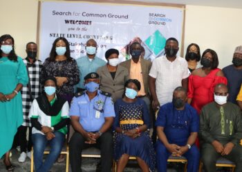 A group of people (five sitting and thirteen standing) indoor wearing a face masks