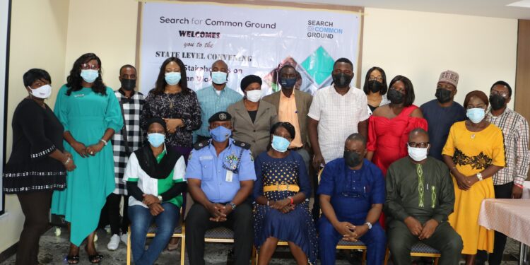 A group of people (five sitting and thirteen standing) indoor wearing a face masks