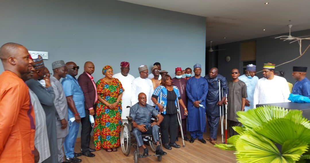 Image of a group of persons standing outdoor. One of them is on a wheel chair