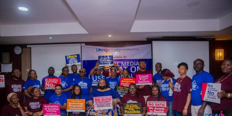 People in a group picture, some are seated while some are standing, most of them are holding placards. The dominant colour is blue