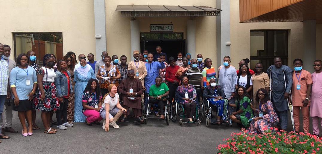 An image of a group of people outside a building, some standing. Four squating and another four on wheel chair. on