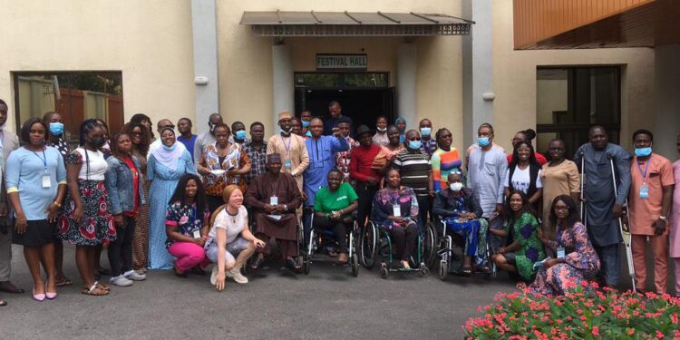 An image of a group of people outside a building, some standing. Four squating and another four on wheel chair. on