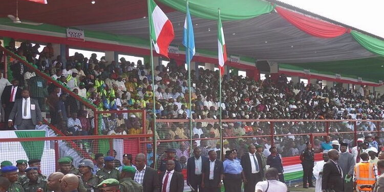 An image of a lot of people gathered outdoor. Some standing others sitting under a shade.