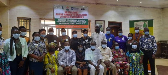People in a group picture, some are sitting while some are standing. There is a banner in the background