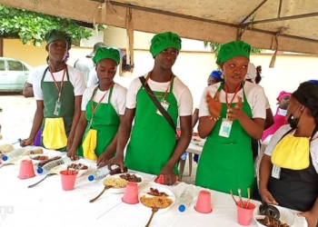 Ladies standing in front of a cooking table, wearing white dresses and green apron and green chef cap