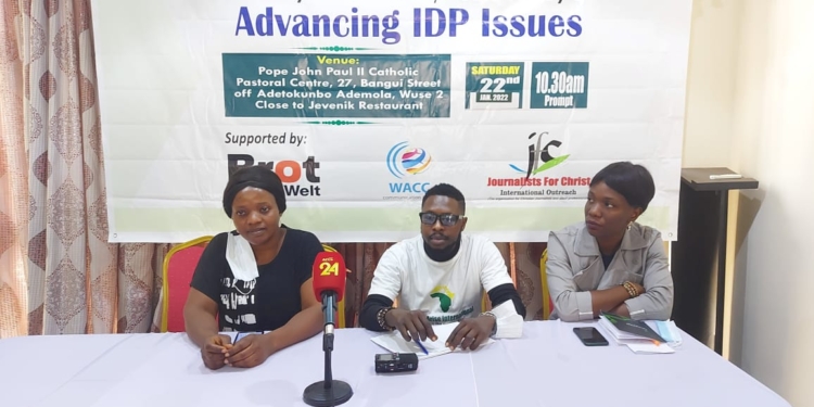 Three persons, a woman on the left, a man in the centre and another woman on the right sitting at a high table indoors. Their hands are on the table and hehind them is a banner of Journalist for Christ with donor logos