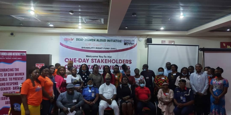 Group of persons standing next to eah other and others sitting next to each other indoor. Behind is a banner with the inscription deaf women aloud initiative