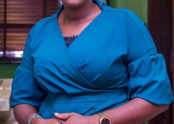 Mrs. Grace Ajayi in a a standing position indoor. Picture is taken from head to waist level. She's leaning on an object and her left palm is on the back on the back of her right hand.