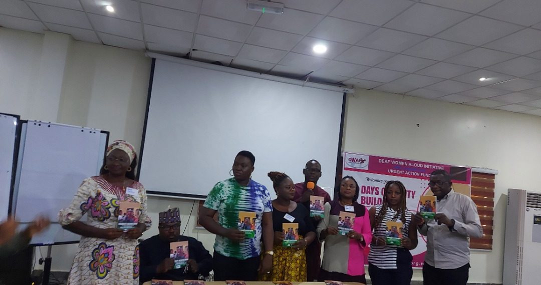 Eight persons standing in front of a table indoors holding books in their hands. Books are also lined up on the table