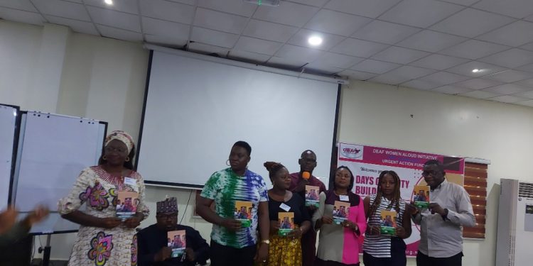 Eight persons standing in front of a table indoors holding books in their hands. Books are also lined up on the table