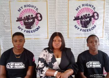 Three people sitting on chair indoor. Two young men in either side and a woman in the middle