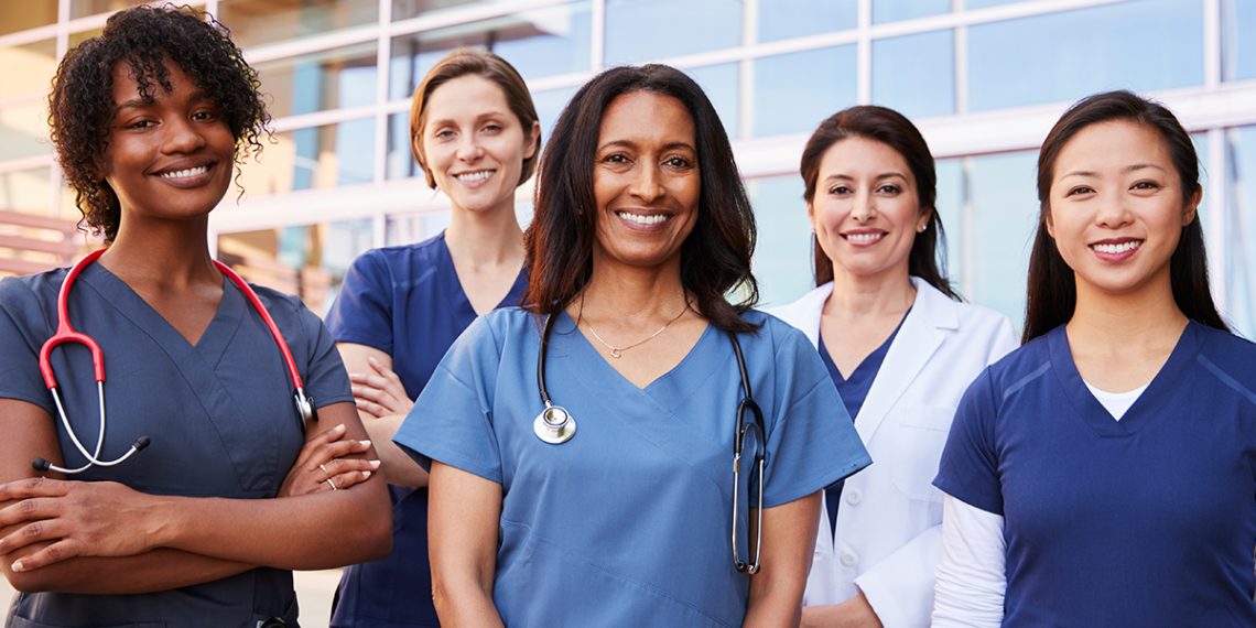 five women standing outdoor on medical outfits. Two have a stethoscope on their neck