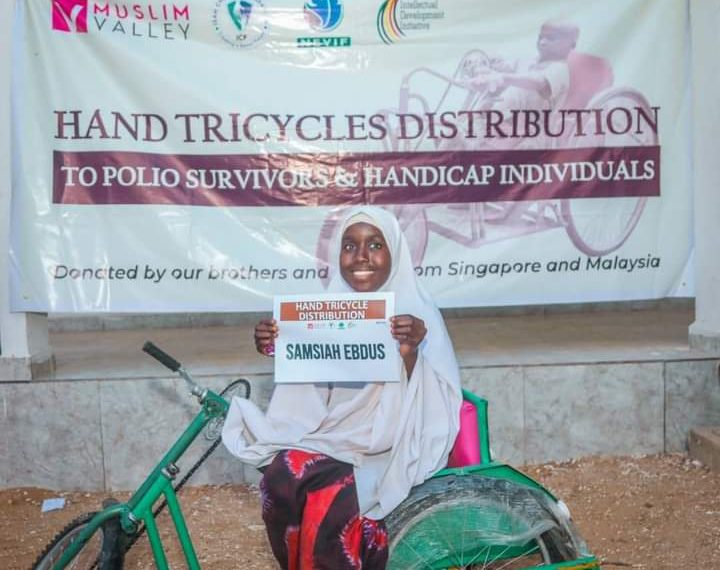 A girl sitting on a hand tricycle and holding a certificate with excitement