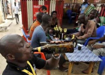 A man holding a bottle of alcoholic drink to his mouth outdoor