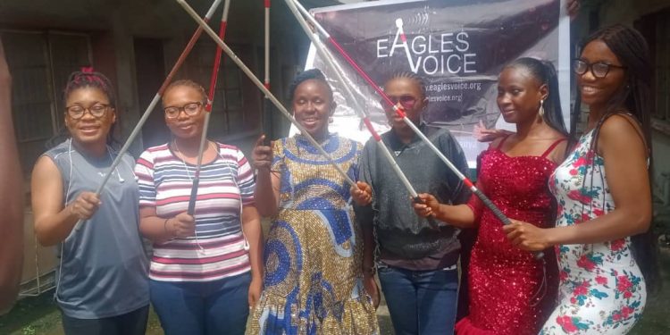 5 women holding their white cane in a group picture. There is a banner in the backgroud. he white canes were raised.