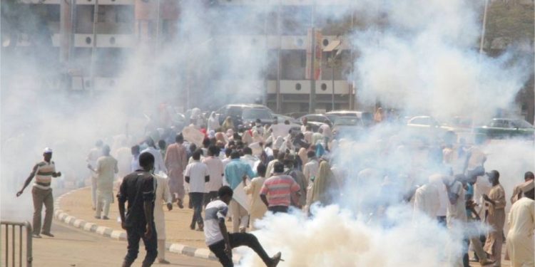 People out on the road running. There is white smoke from a canister on the road