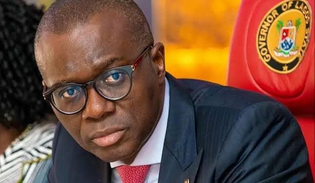 Image of a man on black suit, red tie and glasses sitting indoor.