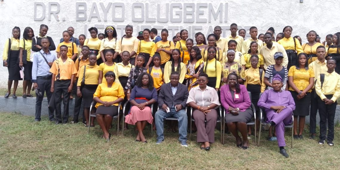 A group of people standing out door. Some are seating in front on a seat