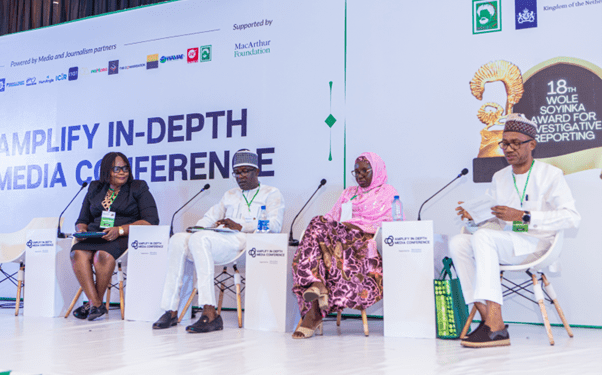 The image of 4 people seated on the stage in a panel discussion.