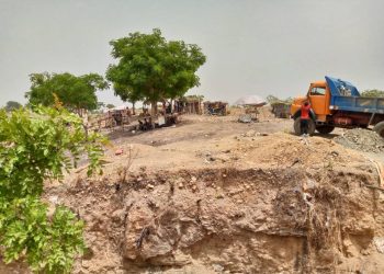 A dry land with few trees and tents scattered around. A tipper truck is packed near one of the trees