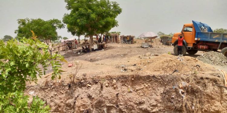 A dry land with few trees and tents scattered around. A tipper truck is packed near one of the trees