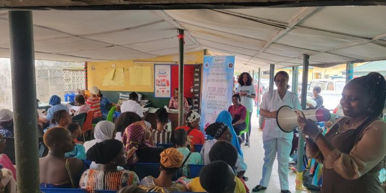 A group of people sitting indoor. One lady is standing holding a megaphone. Two other ladies are also standing in the room.