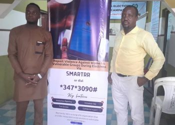 Two men standing indoor in front of a roll up banner