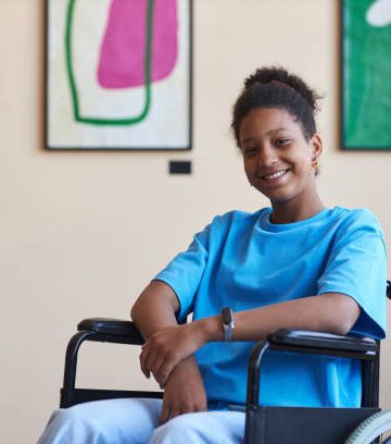 Colorful portrait of black teenage girl with disability smiling at camera while visiting modern art gallery or museum, copy space