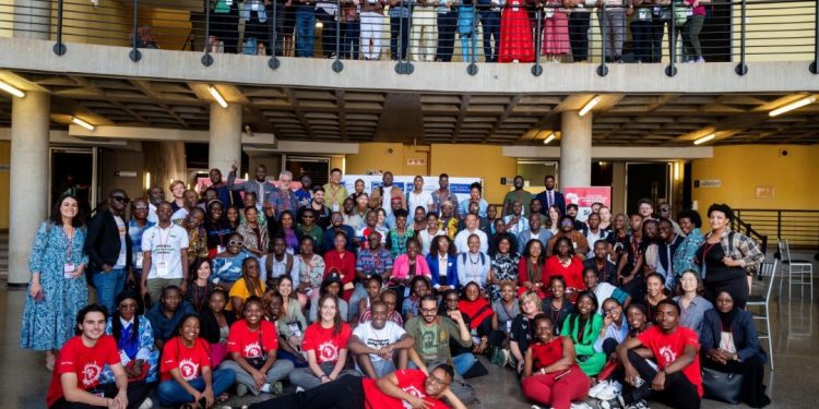 Plenty people standing and sitting indoor. Some are standing on higher ground