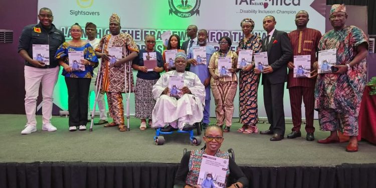 A group of people standing indoor. Two are on a wheel chair. They are each holding a book in their hands