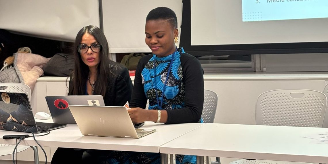 Two women indoor sitting in front of a table with a computer on the table