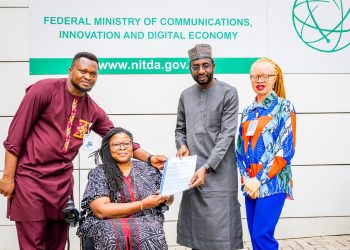 Two men and one woman standing, the other women is on a wheelchair. All are indoor.