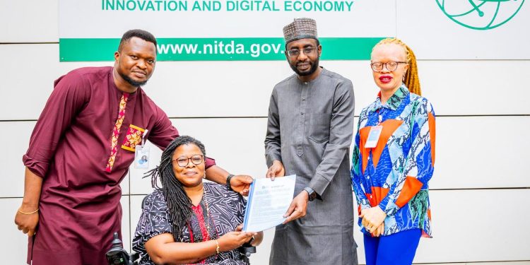 Two men and one woman standing, the other women is on a wheelchair. All are indoor.