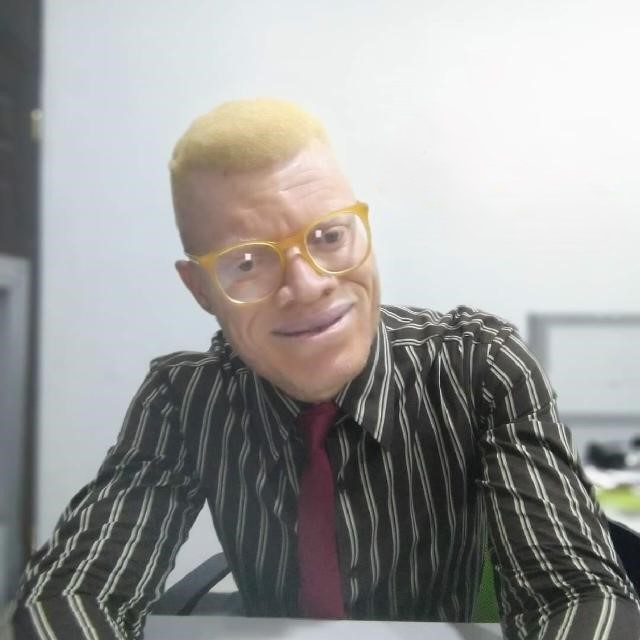 Chest to head view of a man sitting indoor. He is putting on glasses a wearing a tie. 