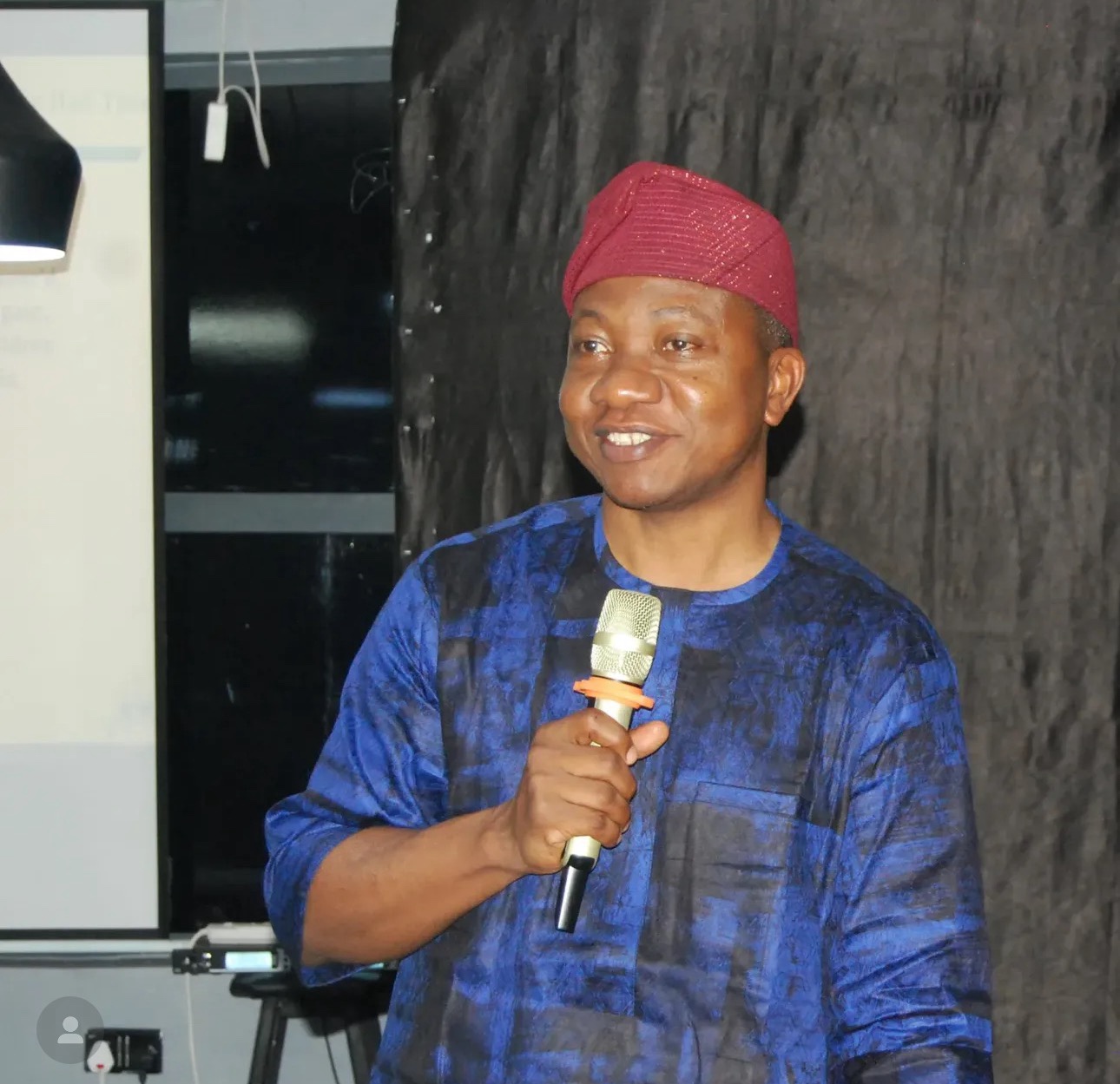 Belly to head shot of a man standing indoors holding a microphone in one hand